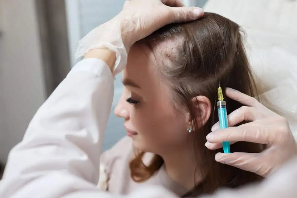 A woman receiving PRP hair restoration treatment as a specialist injects platelet-rich plasma into her scalp to promote hair growth